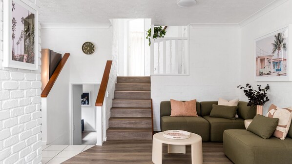 A modern living room with a staircase, a green sofa, and a small round table.