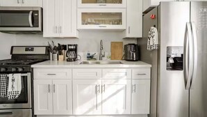 A modern kitchen with white cabinets, a stainless steel refrigerator, a microwave, and a stove.