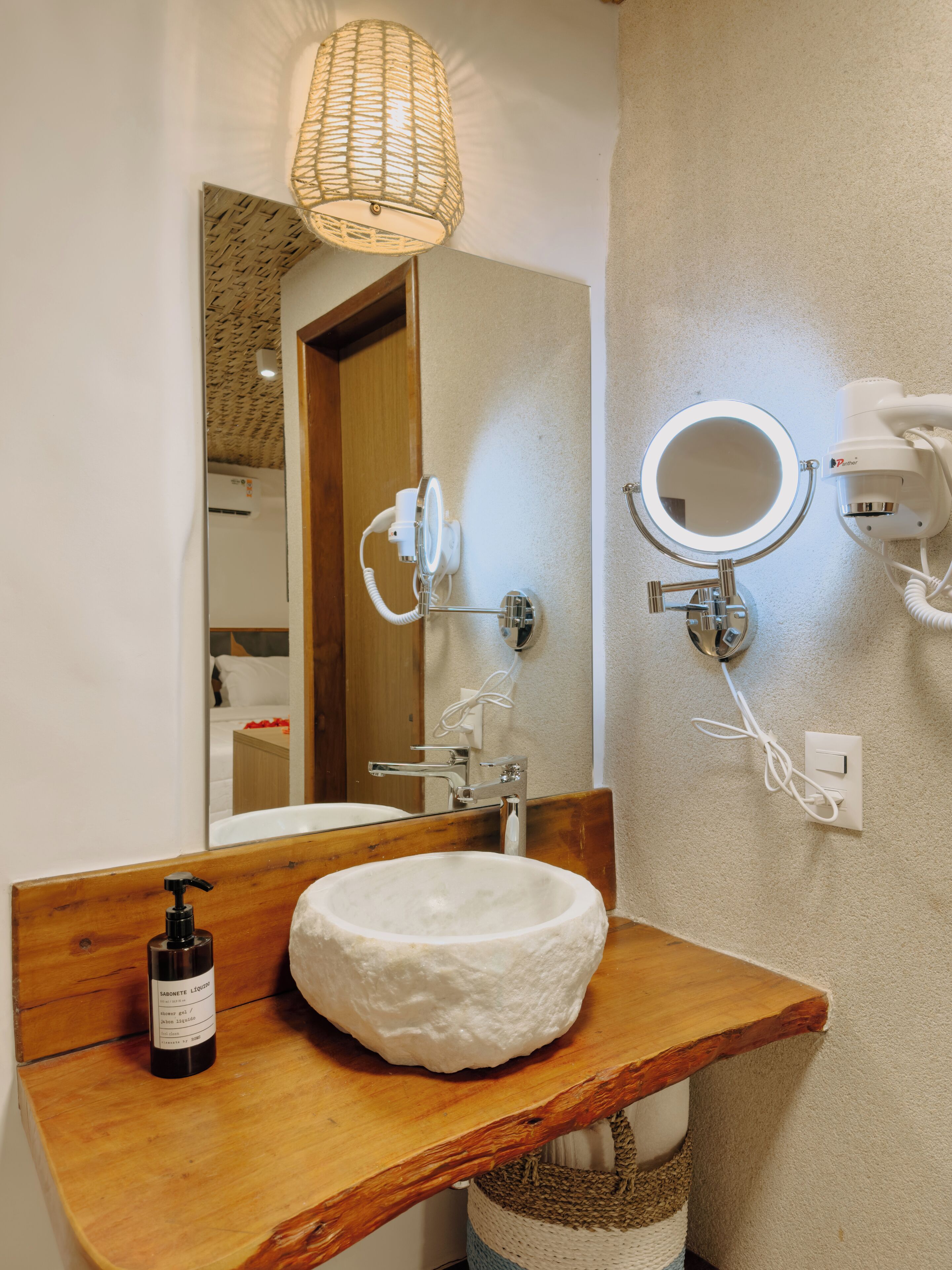 A bathroom with a wooden vanity, a white sink, a mirror, a hairdryer, and a bottle of soap.
