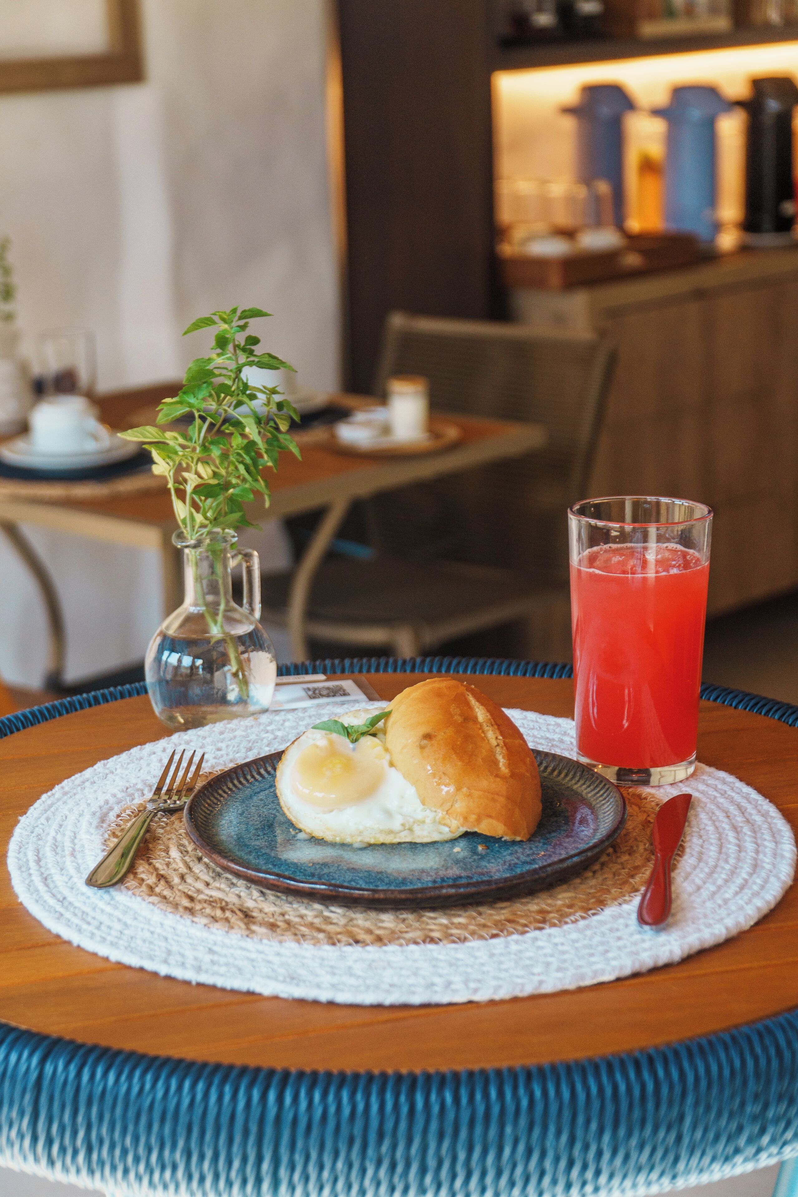 A table with a plate of food, a glass of red drink, and a small plant.