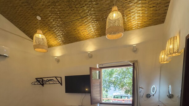A bedroom with a bed, a desk, a television, a window, and a bathroom with a sink and mirror. - Vila de Pedras Noronha (Fernando de Noronha)