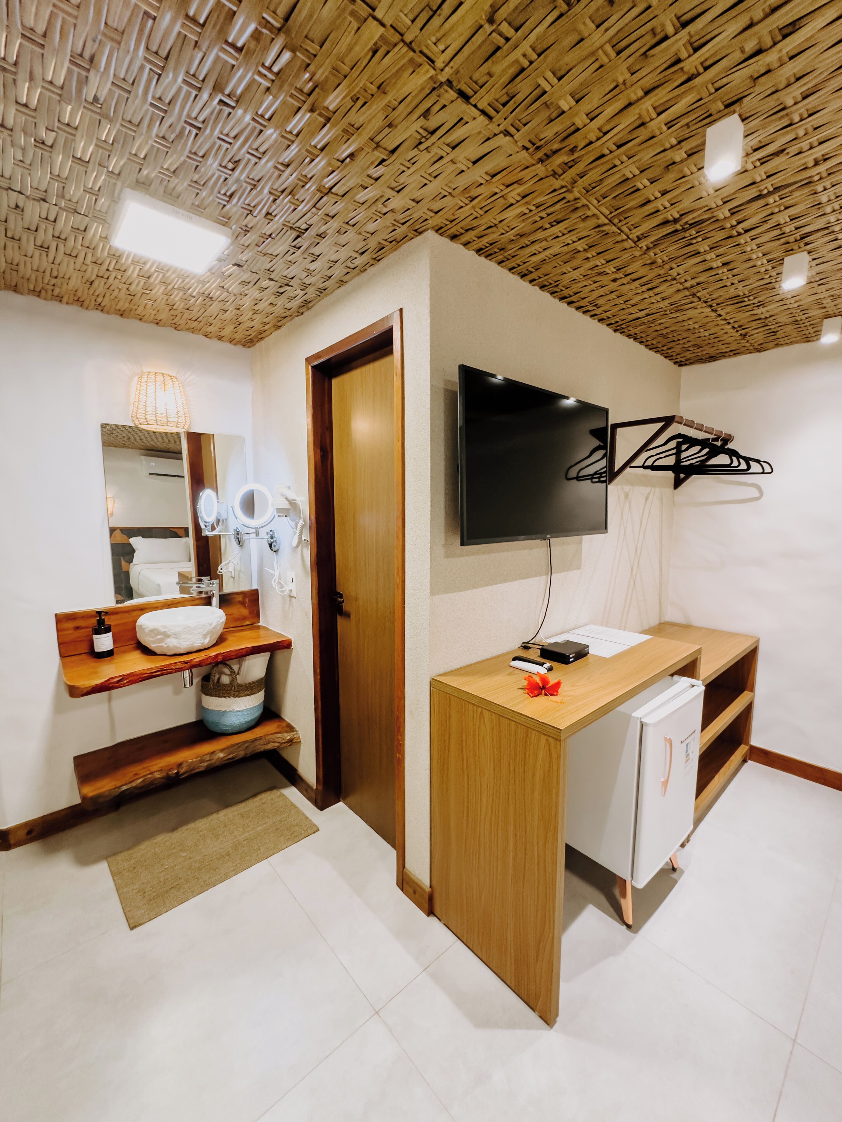 A modern bathroom with a wooden vanity, a mirror, a sink, a toilet, a shower area, and a TV mounted on the wall.