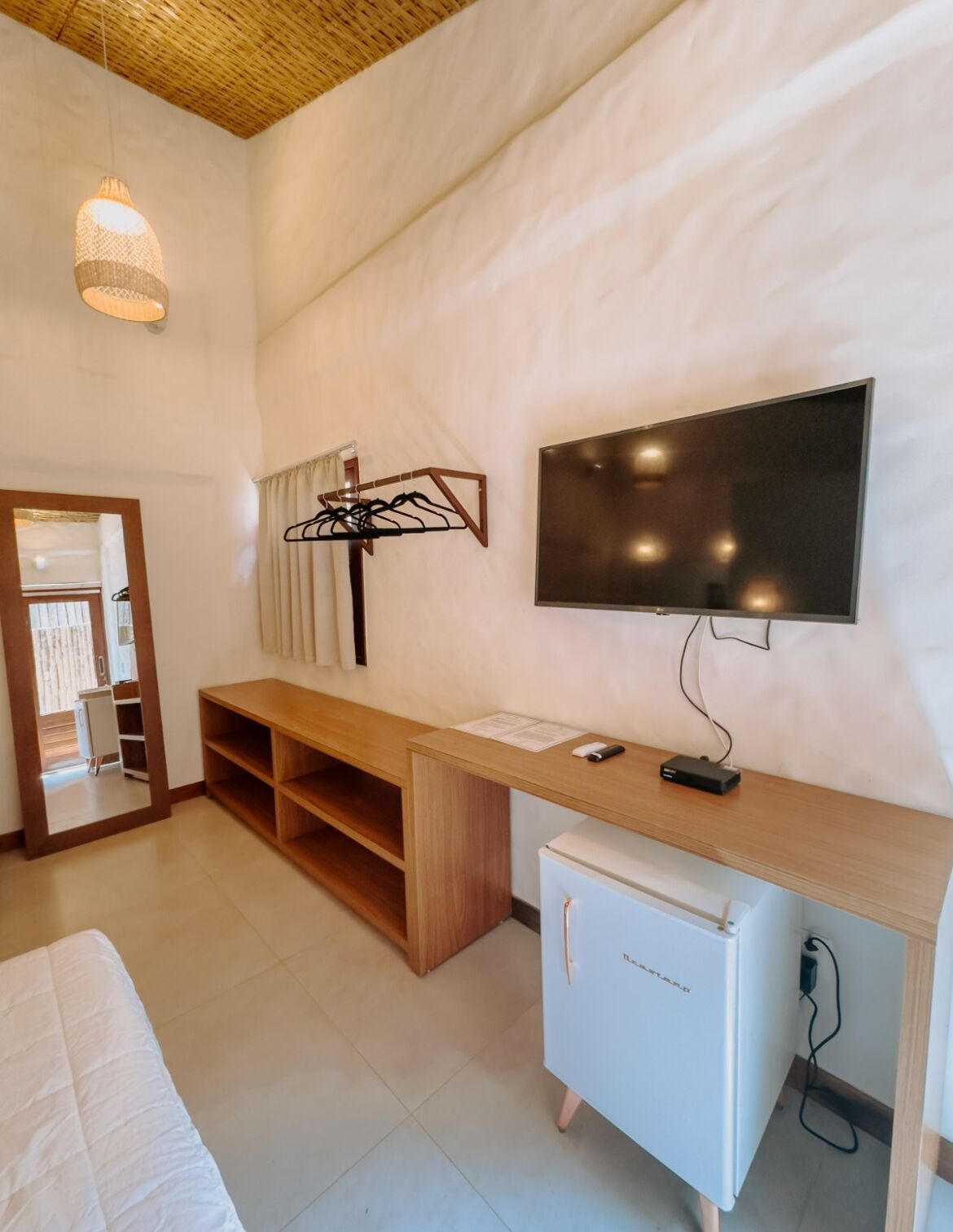 A modern room with a wooden desk, a flat-screen TV, a mini fridge, and a hanging light fixture.