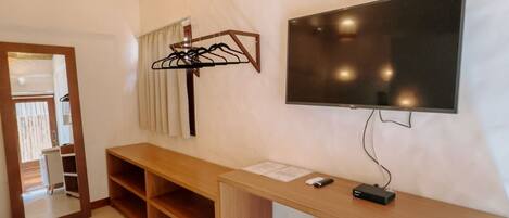 A modern room with a wooden desk, a flat-screen TV, a mini fridge, and a hanging light fixture.