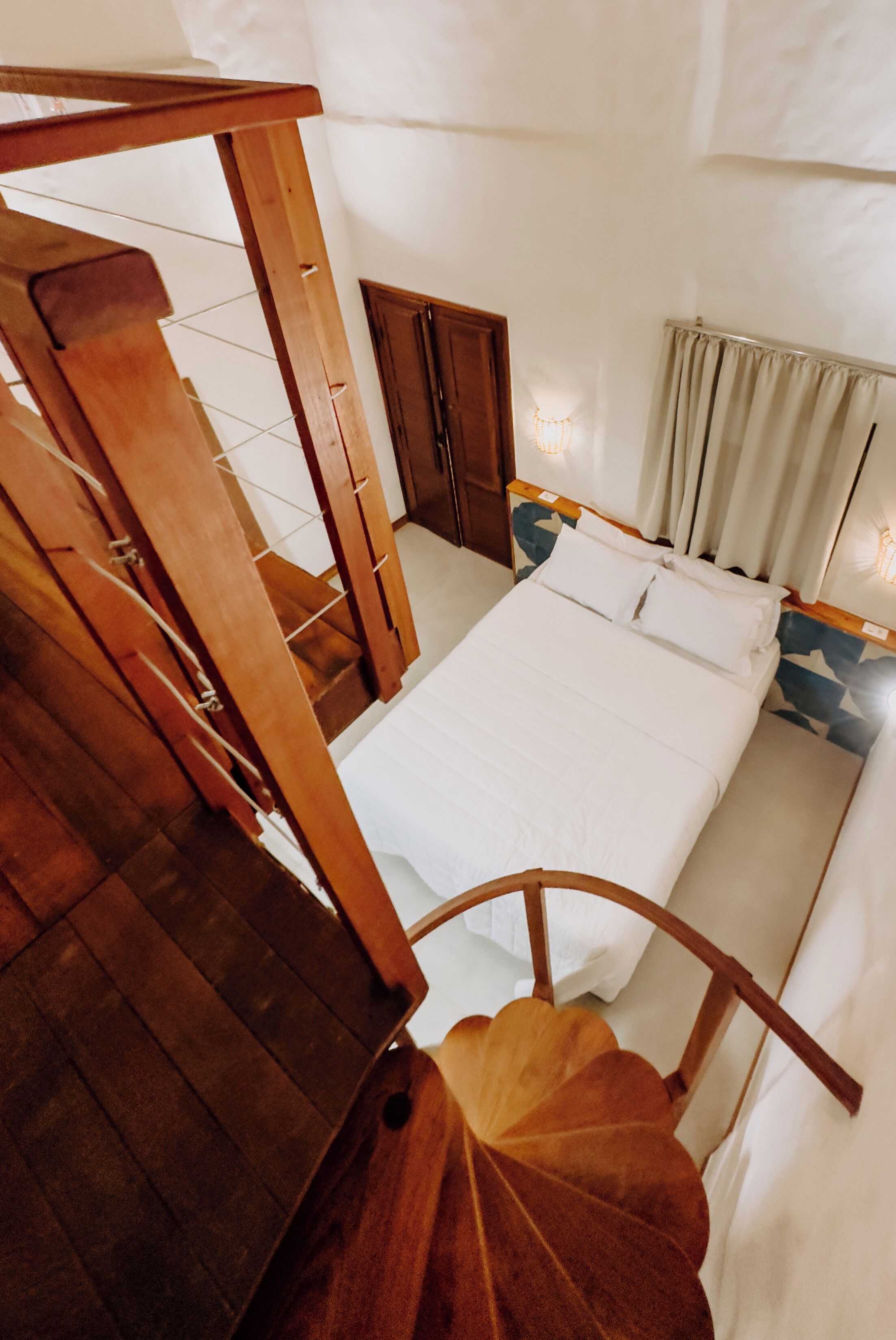 Un dormitorio con escalera de madera, cama con ropa blanca y vista del cuarto.