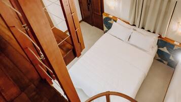 Un dormitorio con escalera de madera, cama con ropa blanca y vista del cuarto.