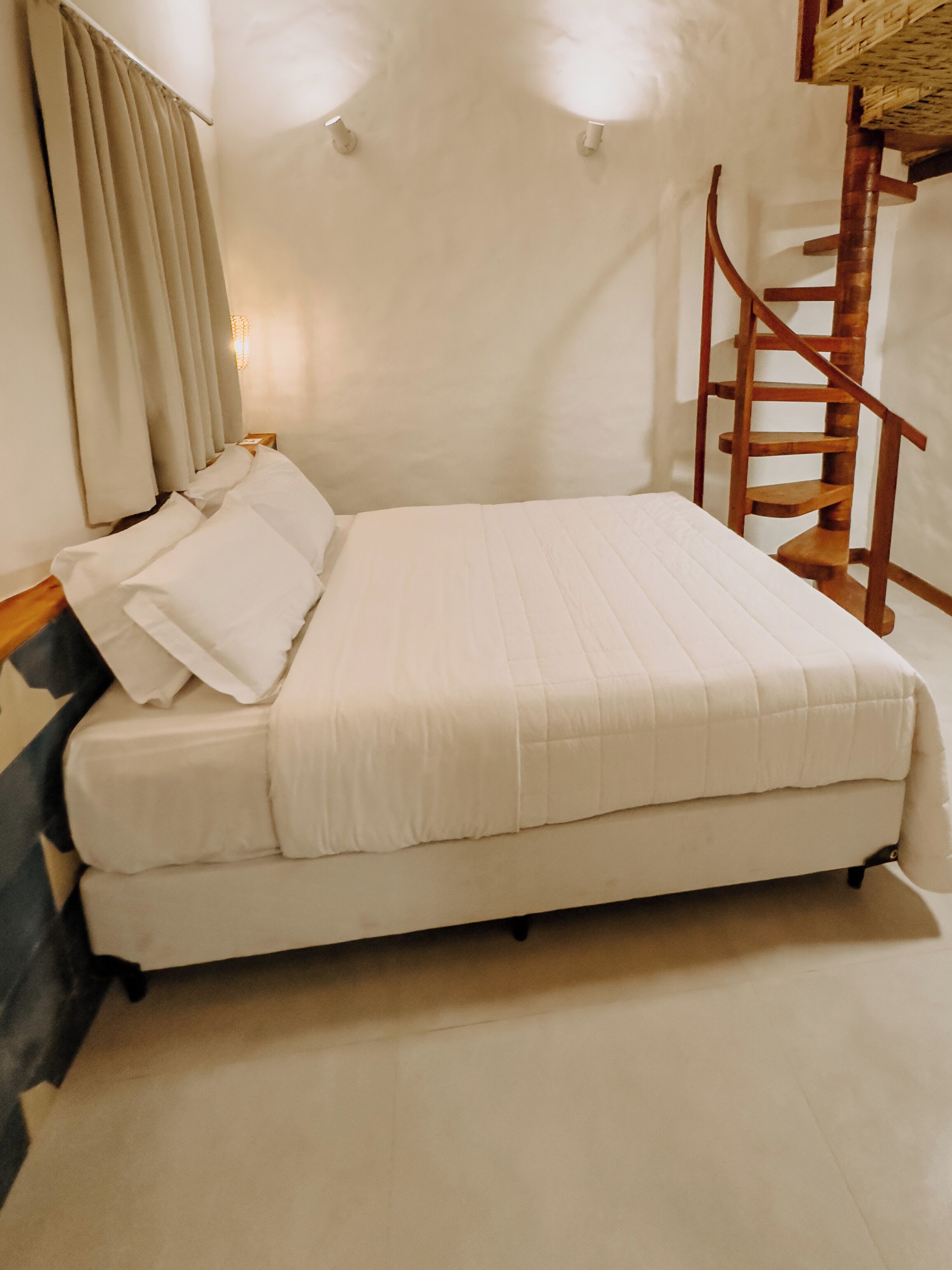 Una cama con ropa de cama blanca, cabecera de madera y una escalera de madera que lleva a un altillo.