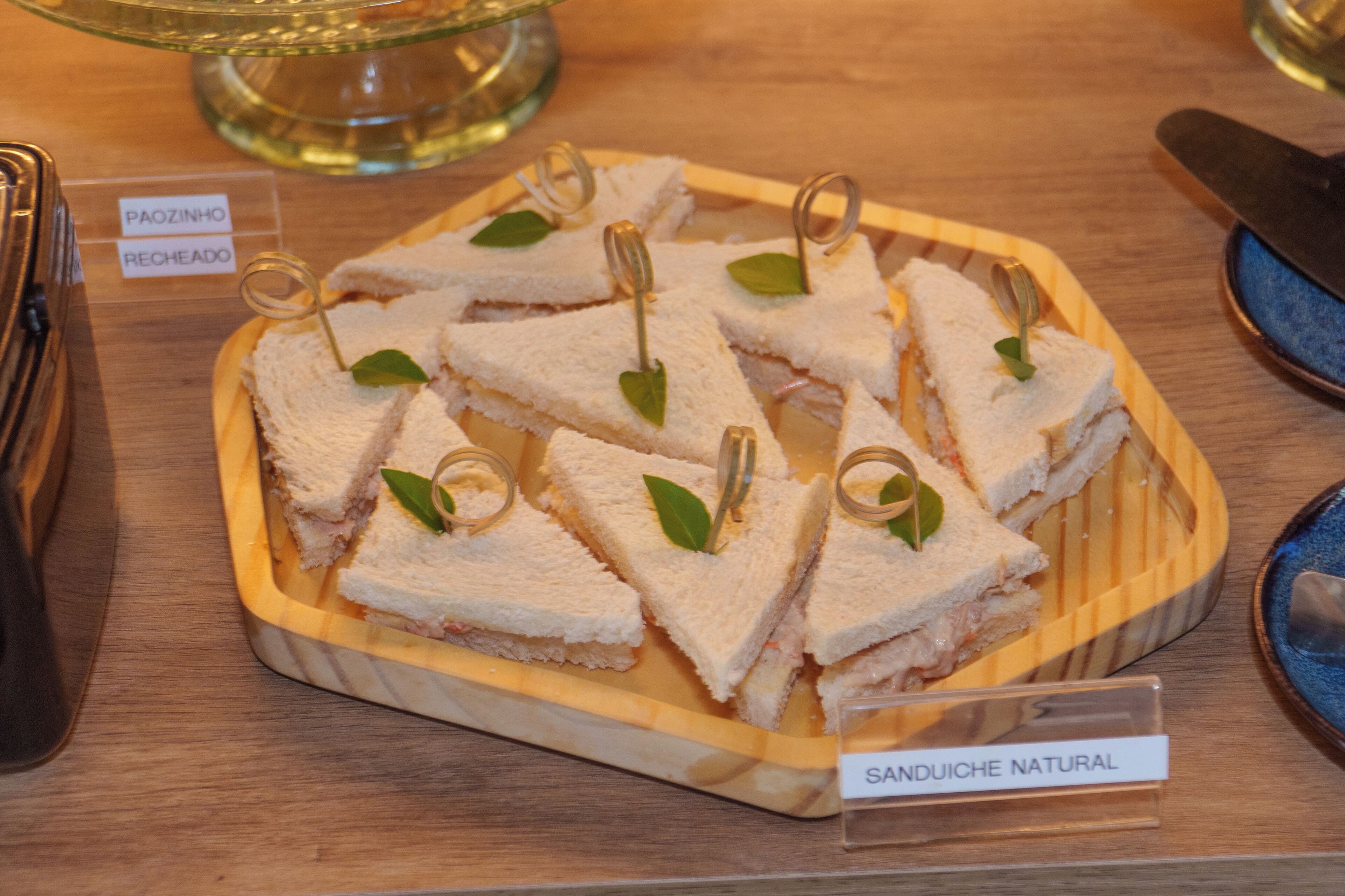 Een houten serveerplank met driehoekige sandwiches, voorzien van de tekst 'SANDUICHE NATURAL'.
