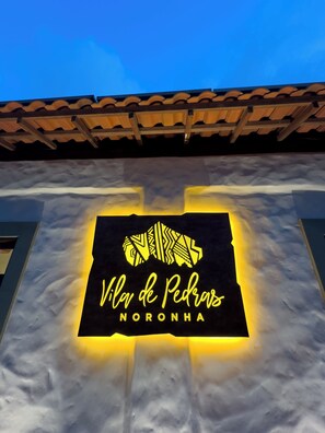 A building with a sign that reads "Vila de Pedra de Noronha" illuminated against a cloudy sky. - Vila de Pedras Noronha (Fernando de Noronha)