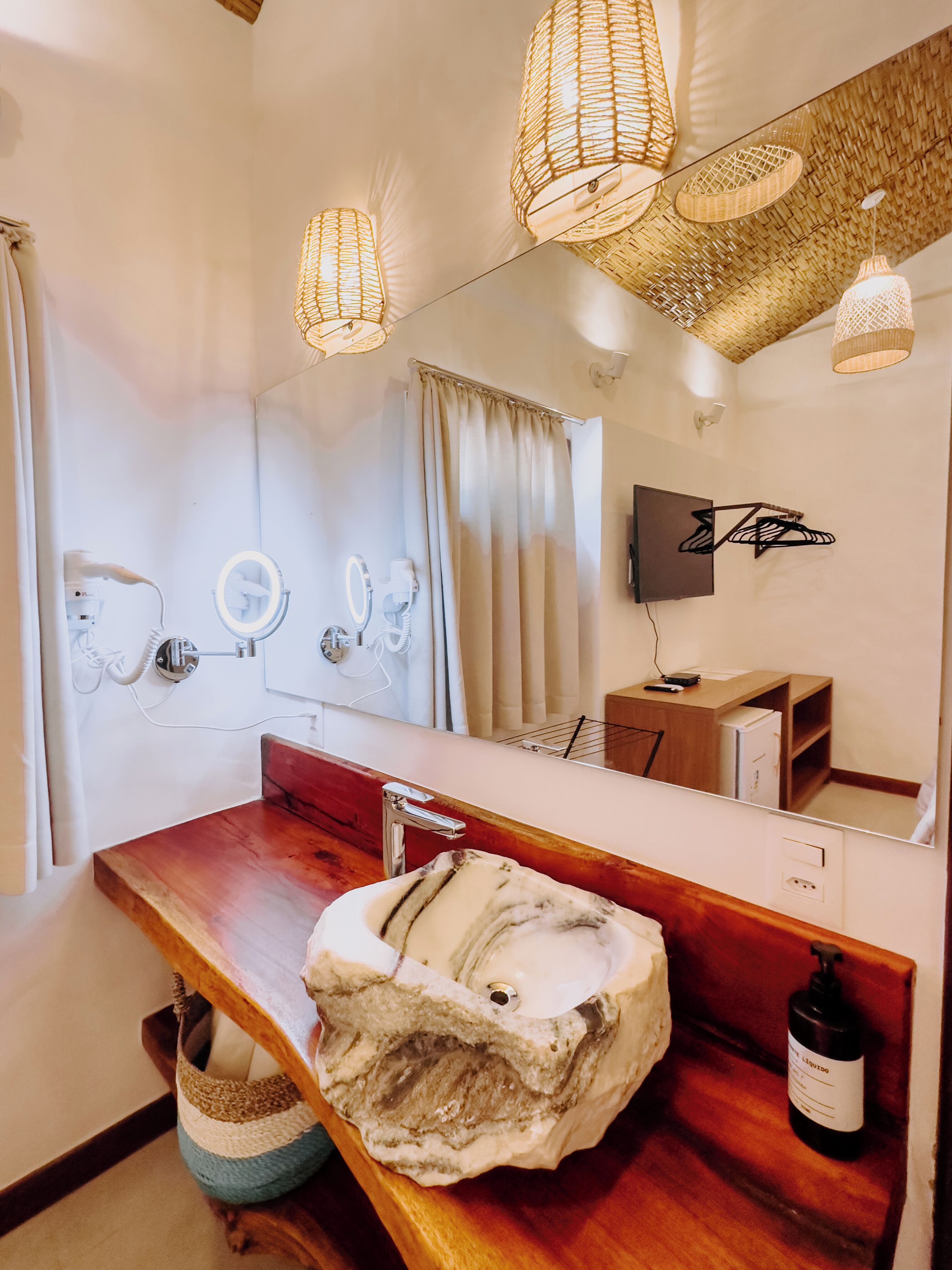 A bathroom with a wooden vanity, a marble sink, a large mirror, and a television mounted on the wall.