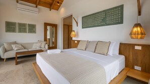 A bedroom with a large bed, a wooden headboard, a wooden bench, a sofa, and a wall-mounted air conditioner. - Villa Bahia (Cóbano)