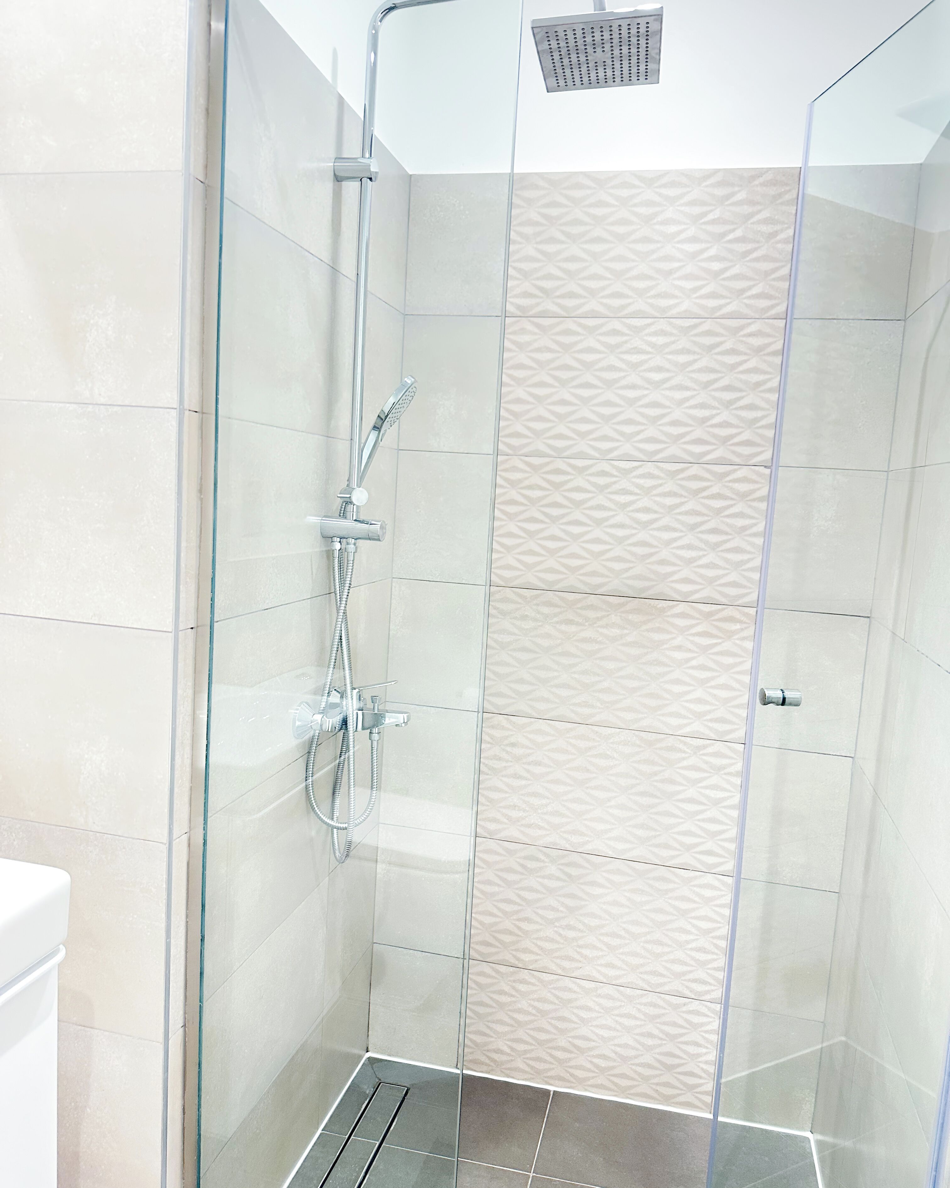 A modern shower enclosure with a glass door, a handheld showerhead, and a wall-mounted control panel.