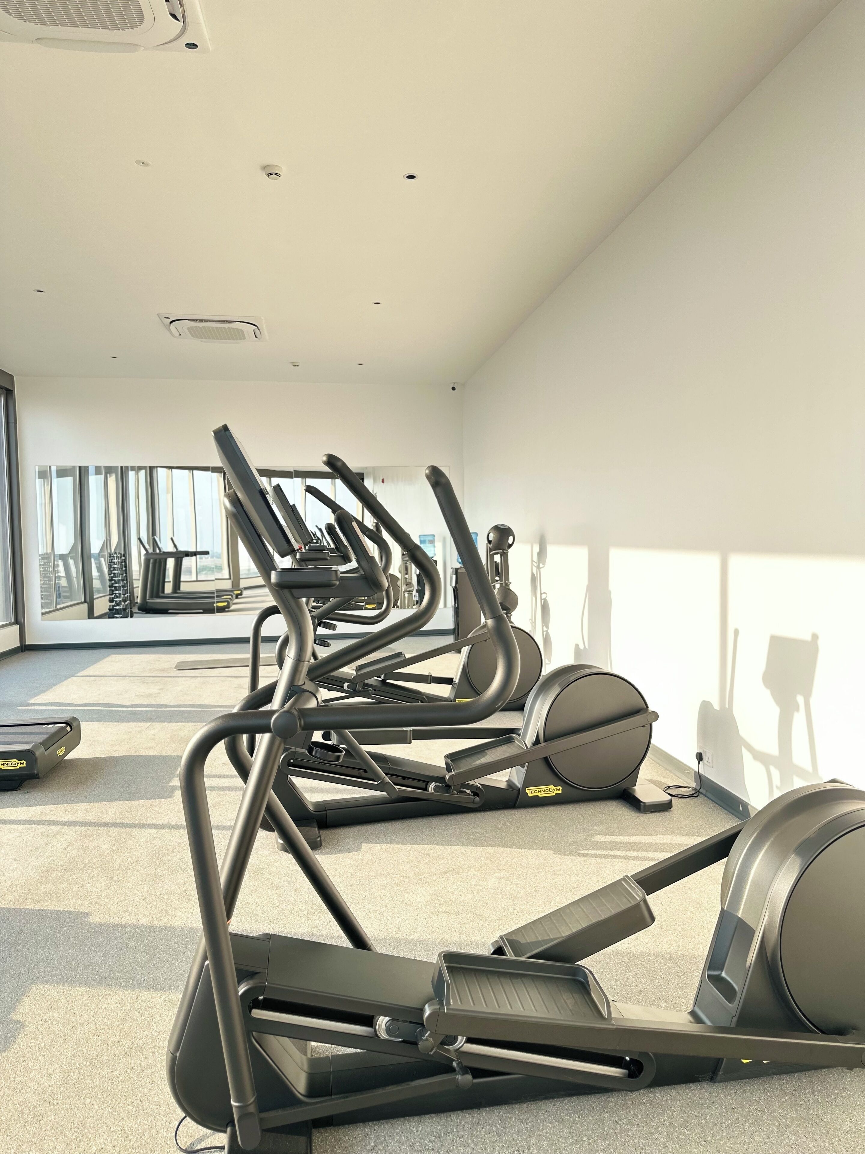 Une salle de sport dotée de nombreux tapis de course et d’appareils d’exercice, de grandes fenêtres et d’un aménagement propre et moderne.