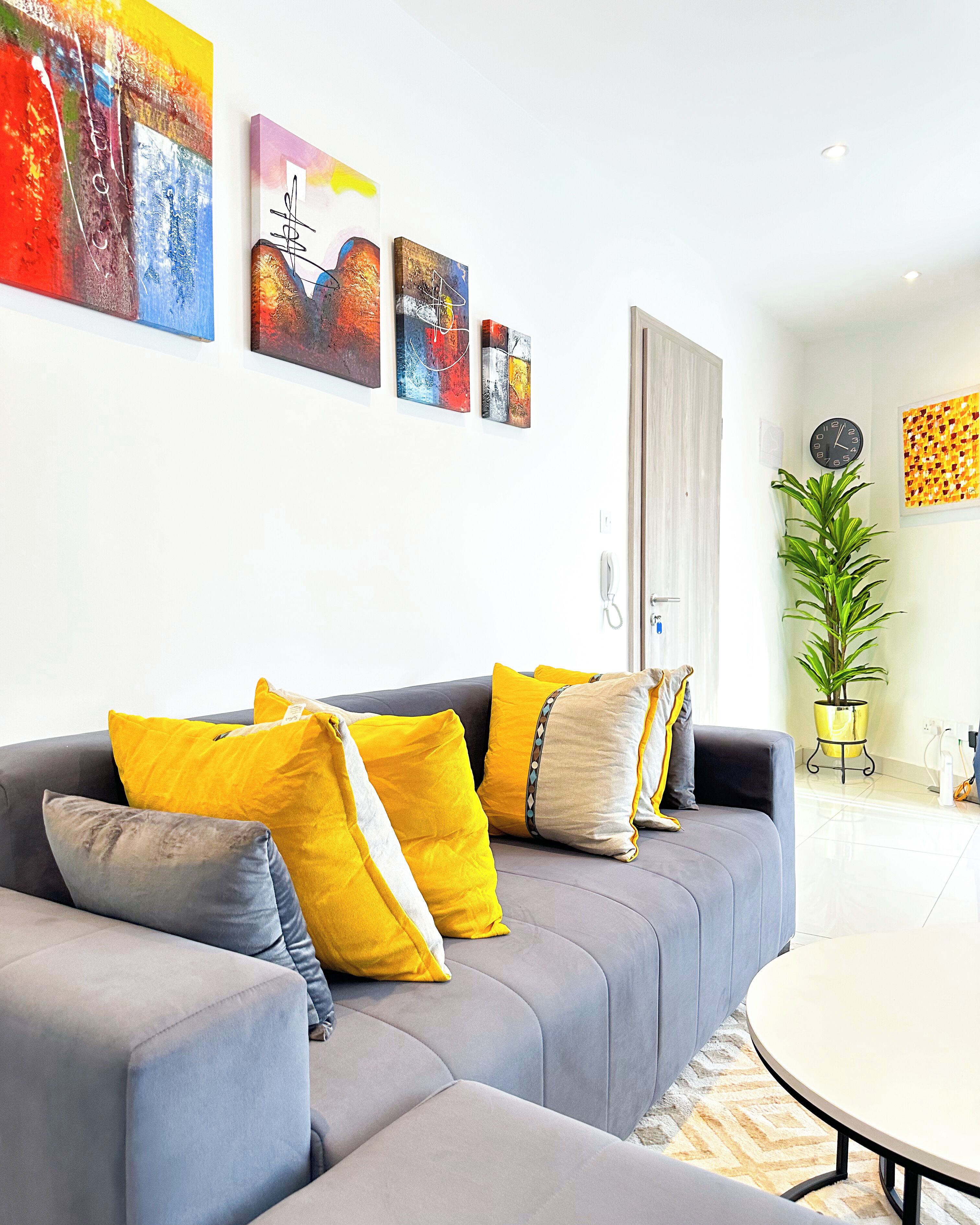 A modern living room with a grey sofa, yellow and grey cushions, and abstract art on the wall.