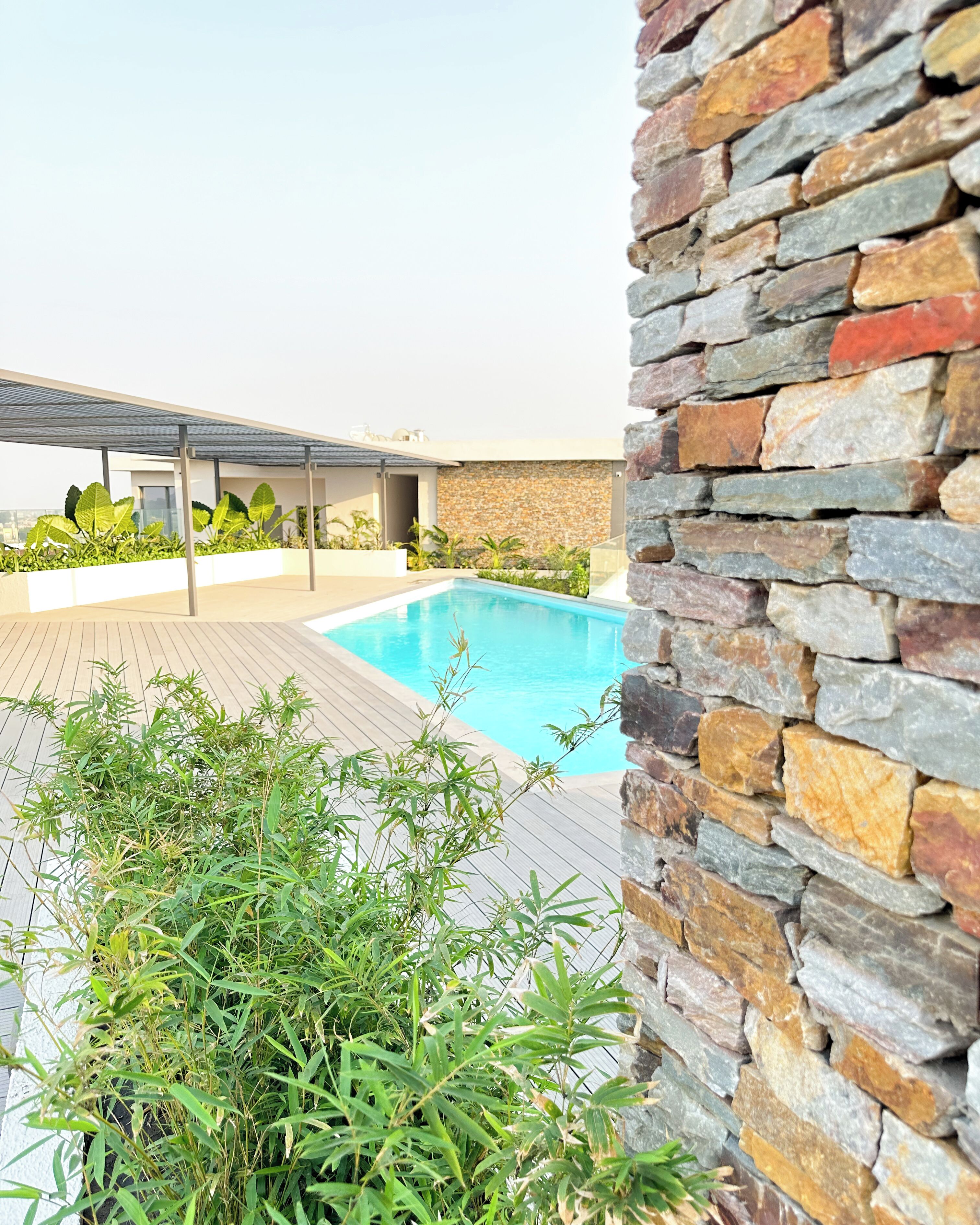 A swimming pool with a stone wall and greenery in the foreground.