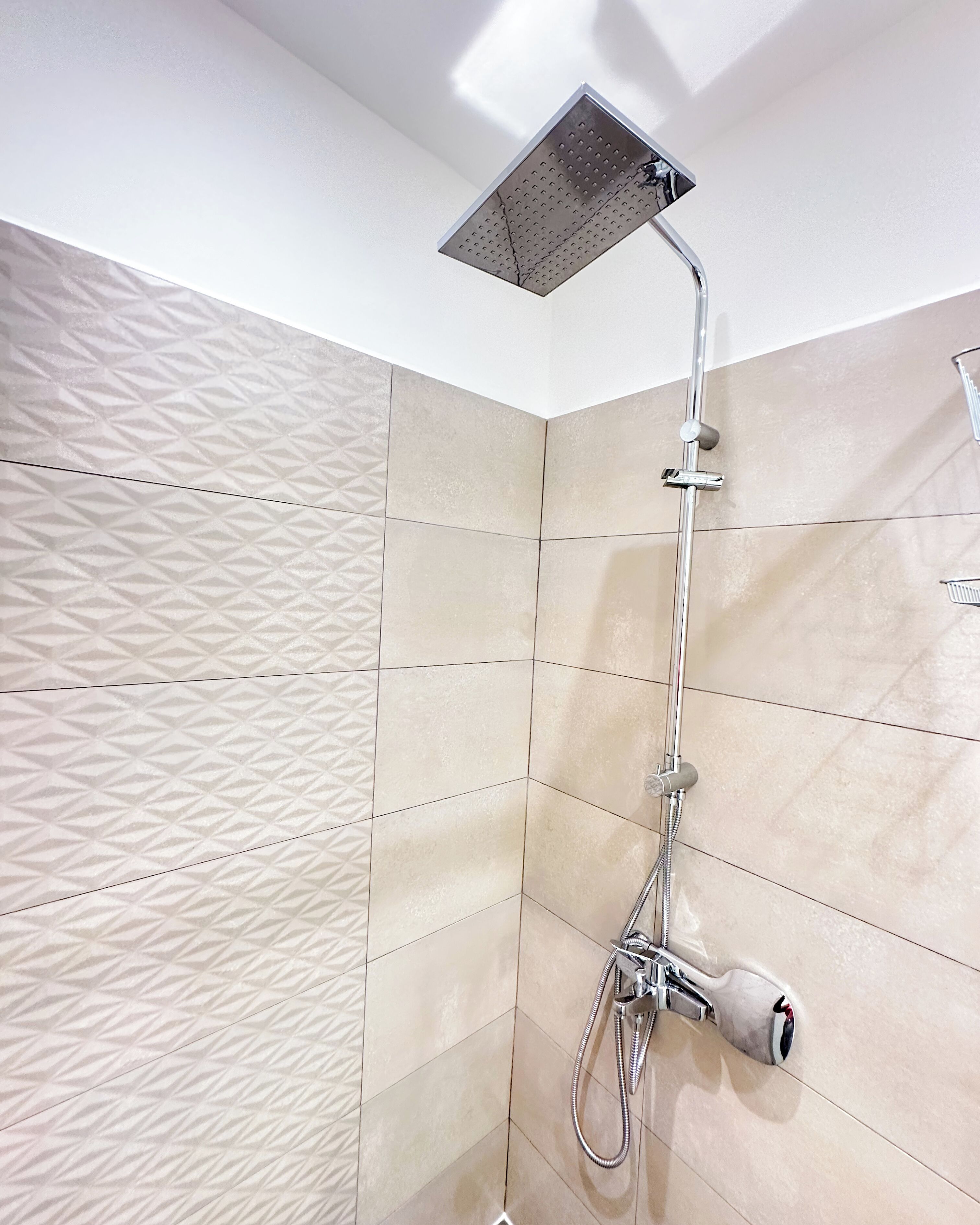 A shower with a handheld showerhead and a fixed showerhead, both mounted on a wall with a geometric tile pattern.