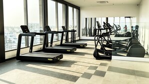 A modern gym with treadmills, elliptical machines, and a large mirror. - Loxwood House Apartment (Accra)