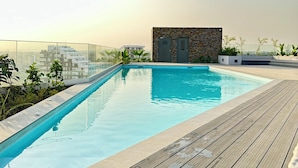 A rooftop swimming pool with a wooden deck, surrounded by greenery and a stone wall. - Loxwood House Apartment (Accra)