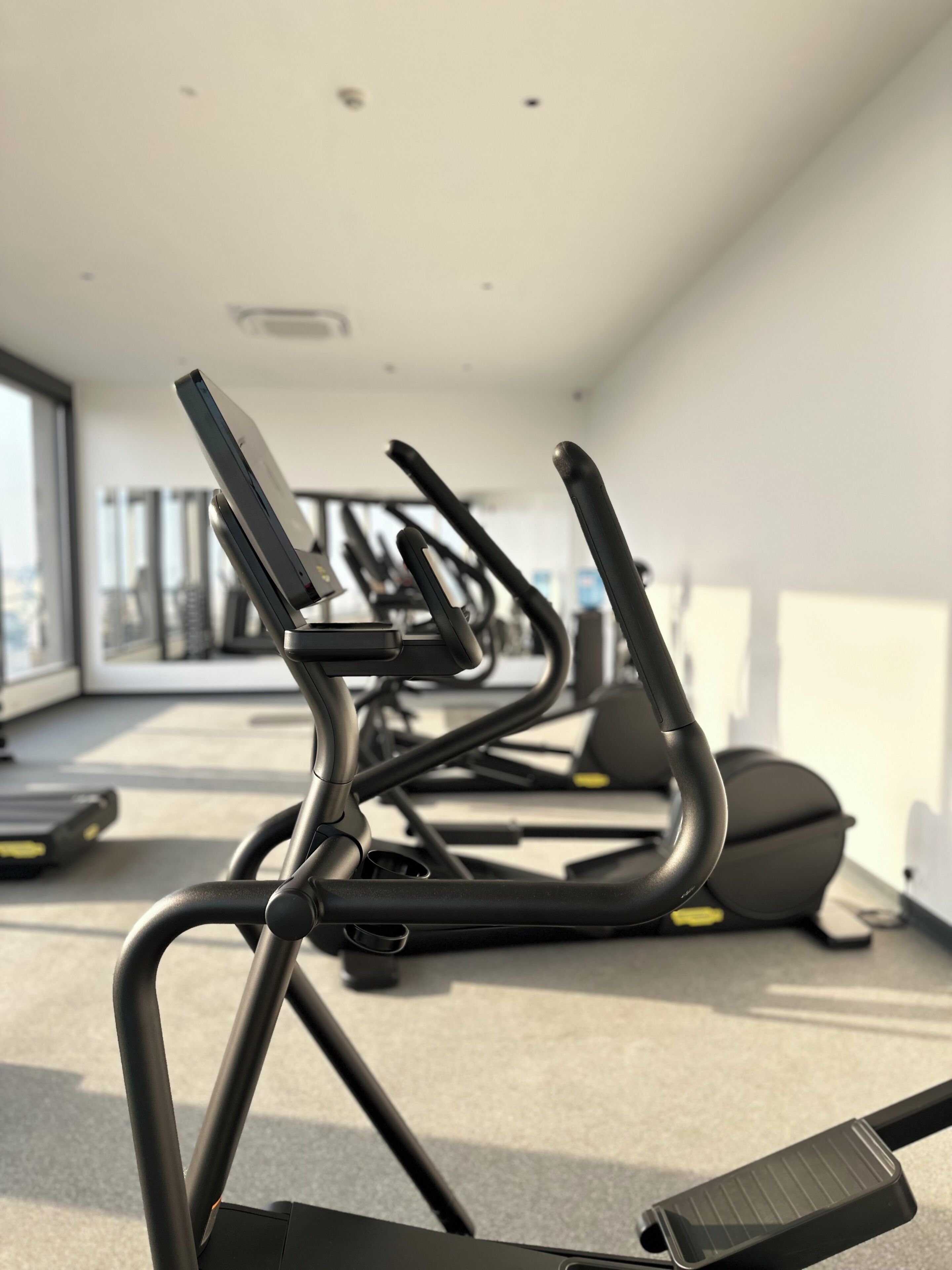 Une salle de sport équipée de vélos d’exercice et de tapis de course, dotée de grandes fenêtres et d’un plafond haut.