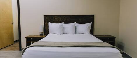 Una cama bien hecha con sábanas blancas y un cabecero de madera, flanqueada por dos mesitas de noche con lámparas.