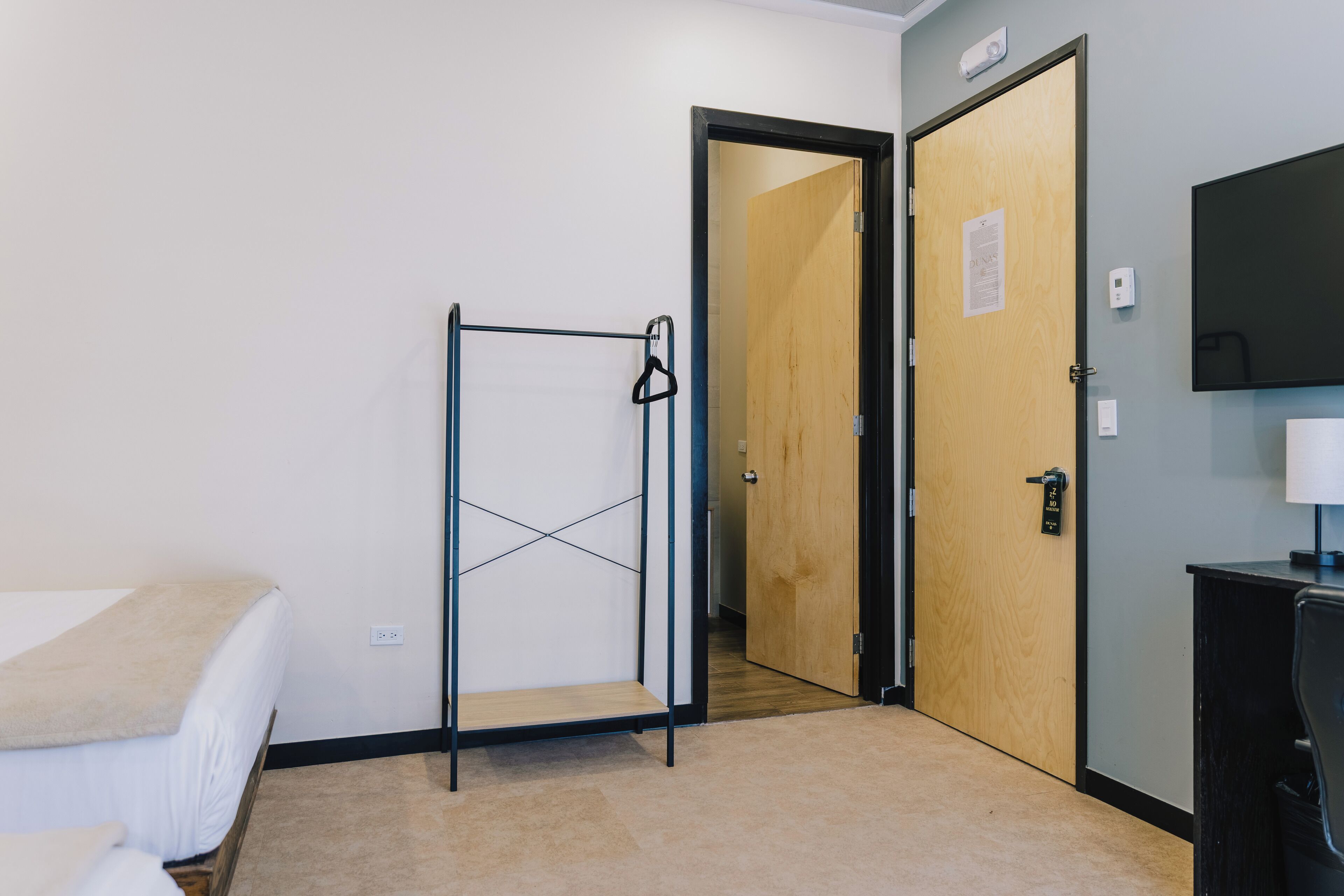 A hotel room with a bed, a metal wardrobe, a wooden door, and a television on a stand.