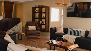 A modern living room with a brown leather armchair, a black sofa, and a wooden coffee table. A dark bookshelf filled with decorative items is in the background. - Hospedaje Consular by Dunas (Ciudad Juárez)
