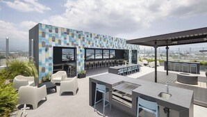 A rooftop bar with a modern design, featuring a patterned wall, outdoor seating, and a view of the city.