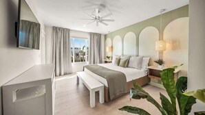 A modern hotel room with a large bed, a bench, a TV, and a balcony with curtains. - Private Beach. ROCK WALL. POOL W/ Zip Line & Slide (Sarasota)