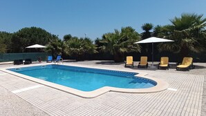 A rectangular swimming pool with a tiled deck, surrounded by lounge chairs and umbrellas.