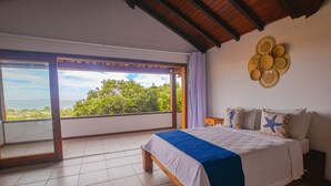 A bedroom with a large bed, a view of the sea, and a ceiling with woven decorations. - Ilha Branca Guest House (Búzios)