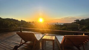 A wooden deck with two lounge chairs and a small table, overlooking a sunset view. - Ilha Branca Guest House (Búzios)