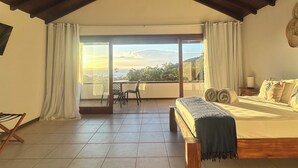 A spacious bedroom with a large bed, a balcony with a view, and a high ceiling. - Ilha Branca Guest House (Búzios)