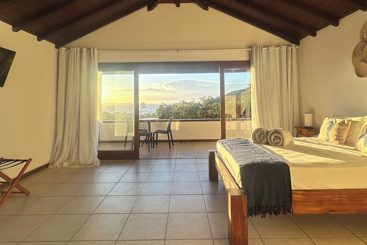 Un dormitorio amplio con una cama grande, un balcón con vistas y un techo alto.