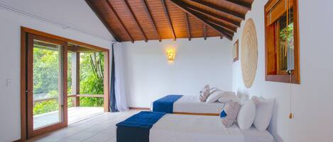 Una habitación amplia con techo alto, una cama grande, una cama secundaria más pequeña y vistas a través de un ventanal corredero.