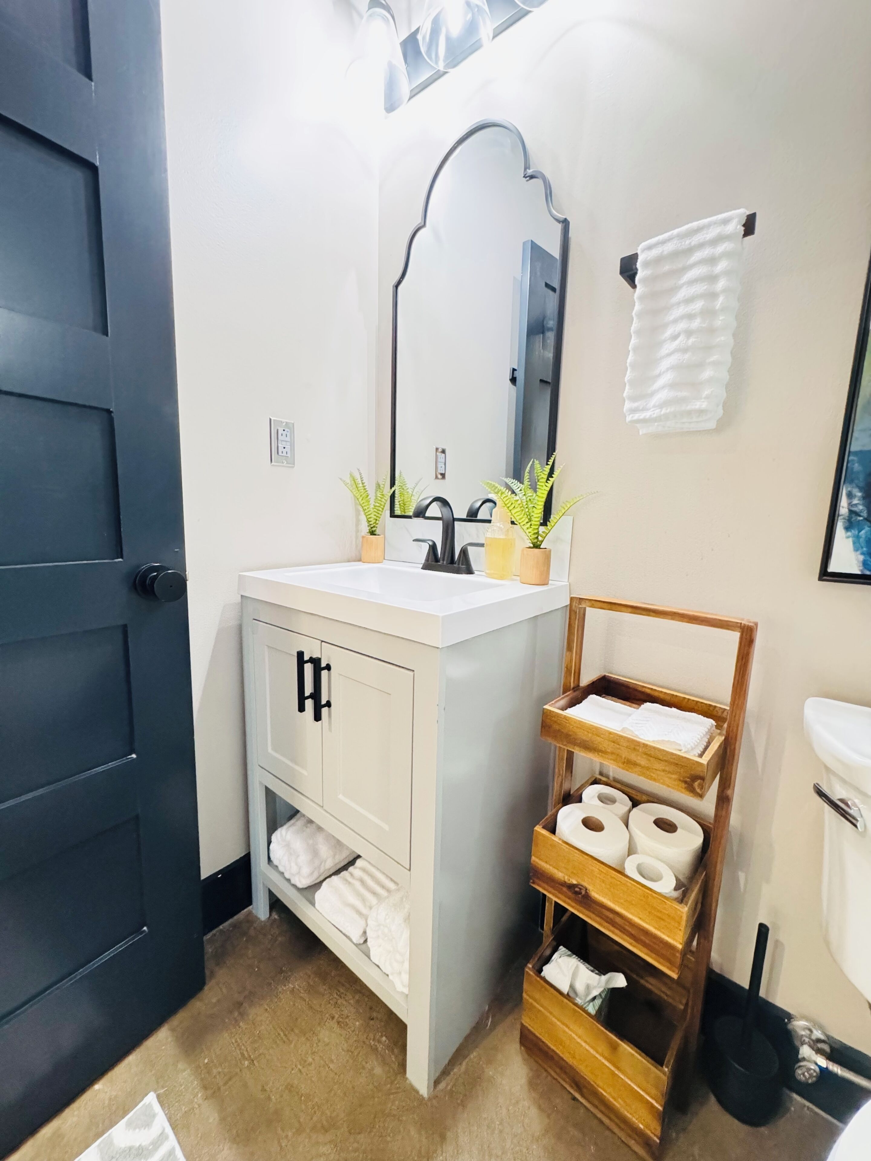 A bathroom with a white sink, black faucet, and a wooden towel rack.