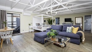 A modern living room with a sofa, a glass coffee table, and a dining area with a table and chairs. - Fisherhaven - Four Bedroom Apartment, Sleeps 8 (Hermanus)