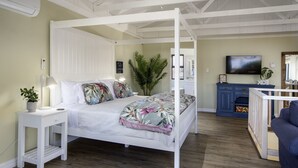 A room with a four-poster bed, a small bedside table with a lamp, a large potted plant, and a TV mounted on the wall. - Fisherhaven - Four Bedroom Apartment, Sleeps 8 (Hermanus)
