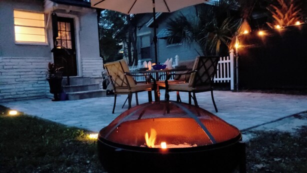 An outdoor patio with a fire pit table and chairs, a white picket fence, and a house in the background. - 2BR/1BA near Jax Zoo -- Welcome, Train Enthusiasts!!  (Jacksonville)