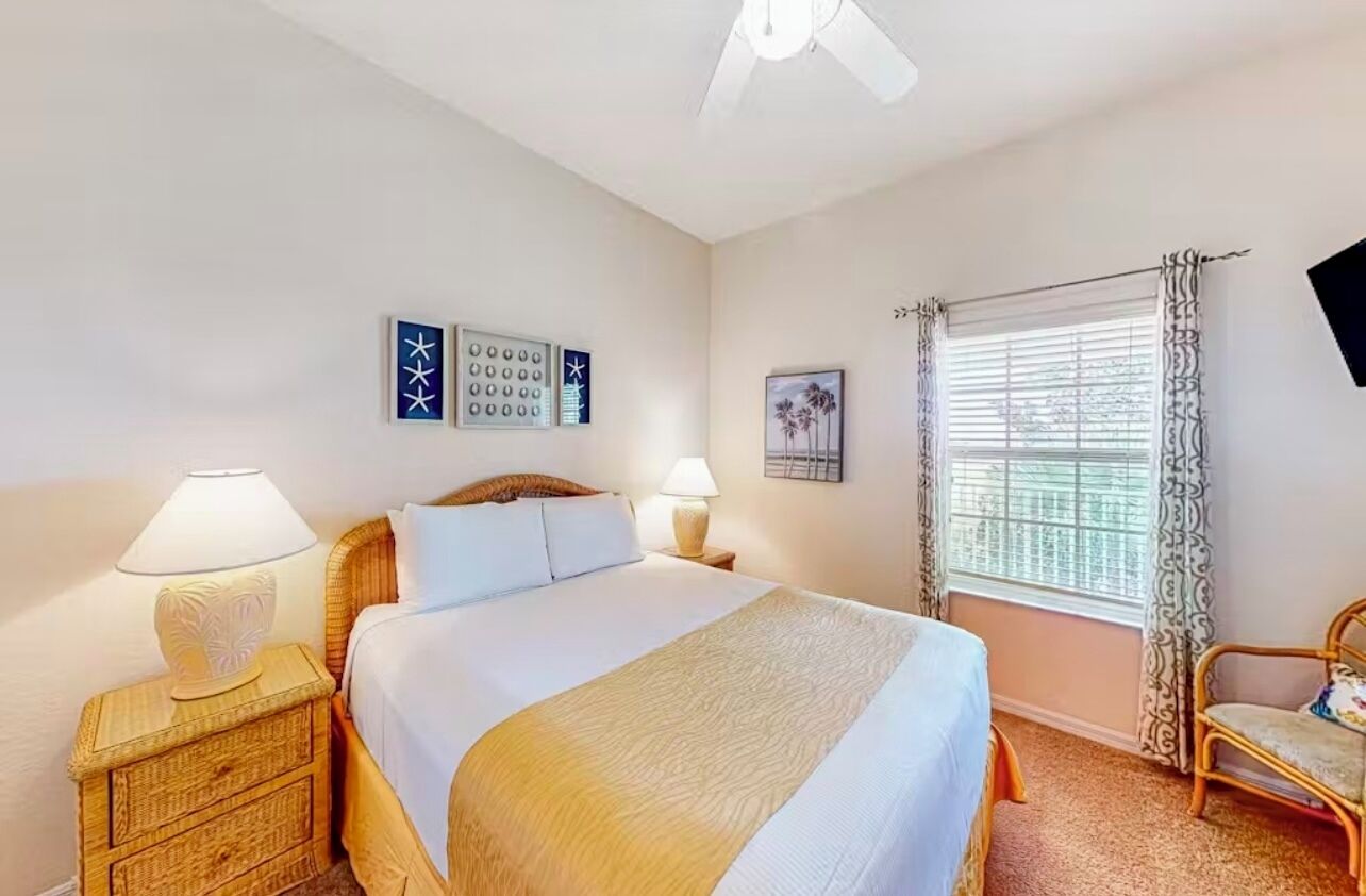 A bedroom with a bed, two bedside lamps, a window with curtains, and wall art.