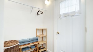 Ett rum med en vit dörr, en hylla i trä, en korg av rotting och en bänk med hopvikta kläder.