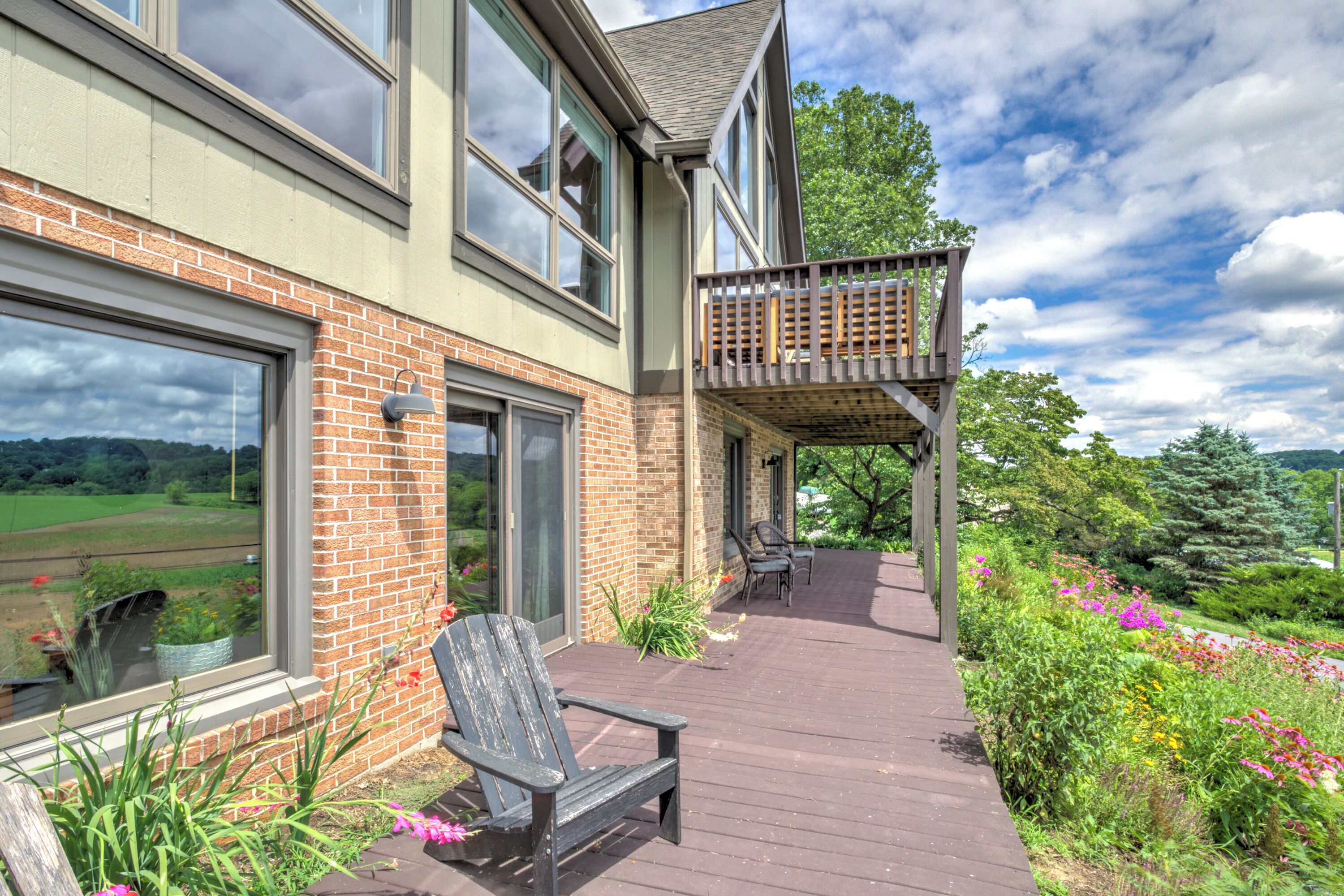 A two-story house with a wooden deck, a covered outdoor seating area, and a view of a green landscape.