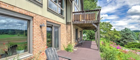 A two-story house with a wooden deck, a covered outdoor seating area, and a view of a green landscape.