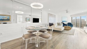 Een moderne woonkamer met een glazen eettafel, transparante stoelen, een bank en een groot raam met uitzicht op de stad.