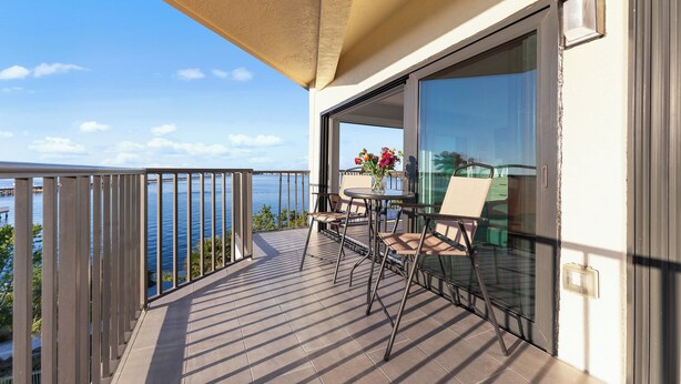 Een balkon met een tafel en stoelen, en uitzicht op zee, met een glazen deur.