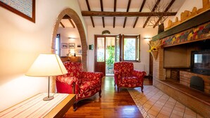 A cozy living room with a fireplace, wooden beams, and red patterned chairs.