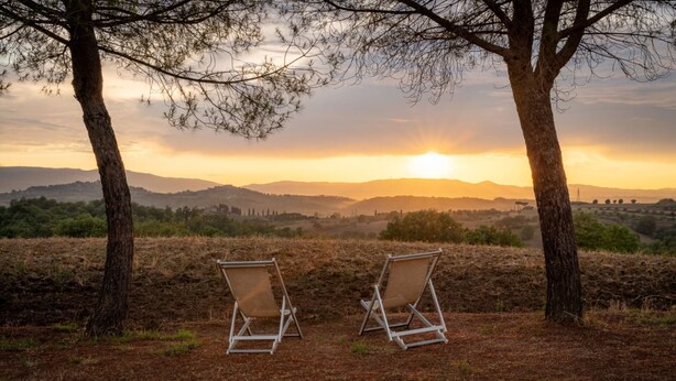 Two empty lawn chairs facing a sunset over a hilly landscape.