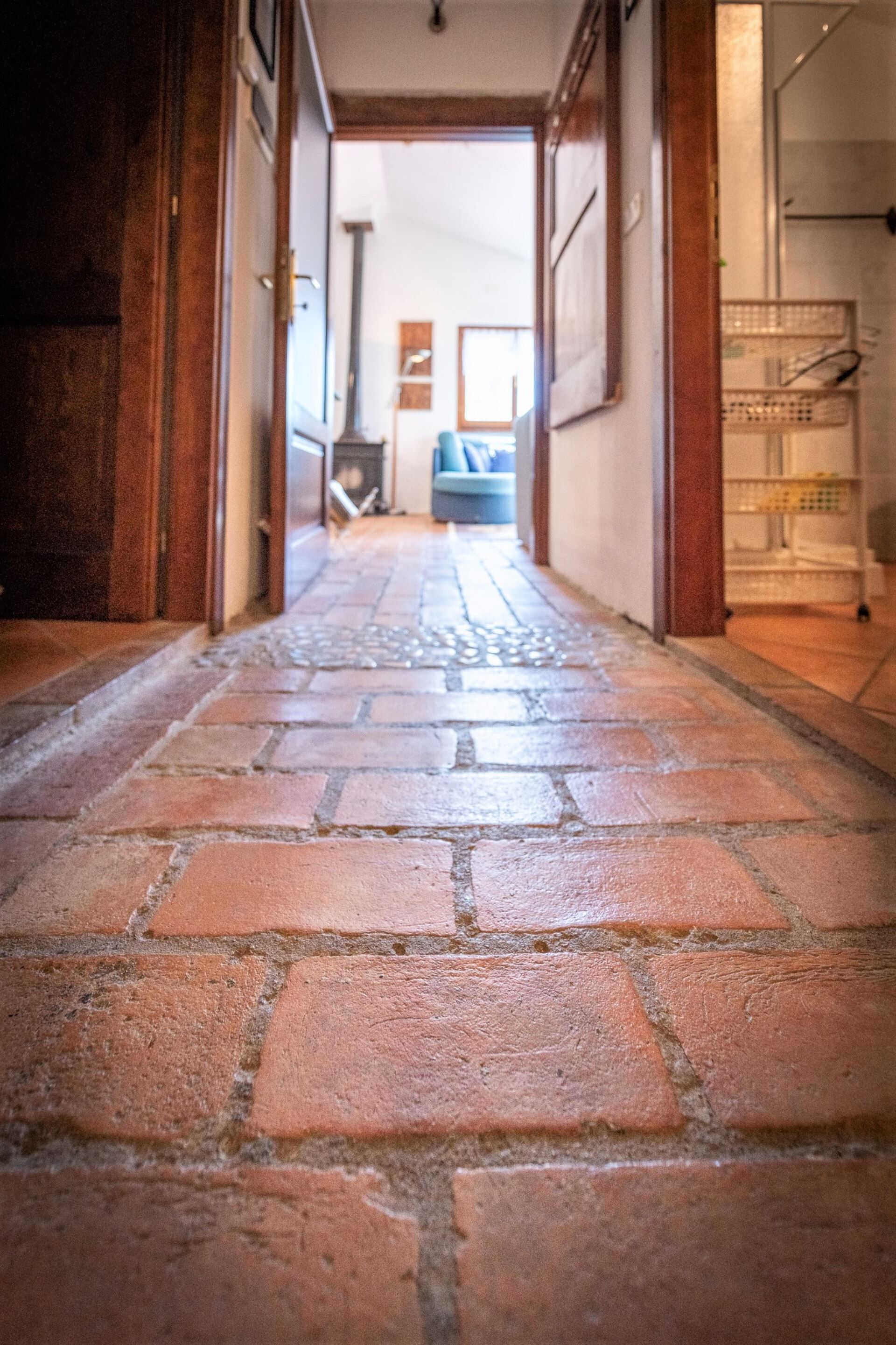 A corridor with a brick floor leading to a room with a bed and a window.