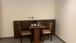 A corner dining area with a wooden table and two chairs. There are plates, cups, and a kettle on the table. - Helat hotel (Al Khobar)