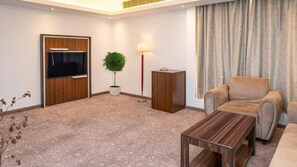A modern living room with a flat-screen TV, a potted plant, a lamp, a wooden cabinet, and a beige sofa. - Helat hotel (Al Khobar)