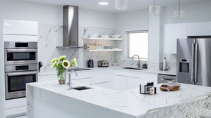 A modern kitchen with white cabinetry, a central island, stainless steel appliances, and pendant lighting. - Charming 2-bedroom villa with AC, WiFi in tranquil Osbourn-Fitches Creek  (St. Georges)
